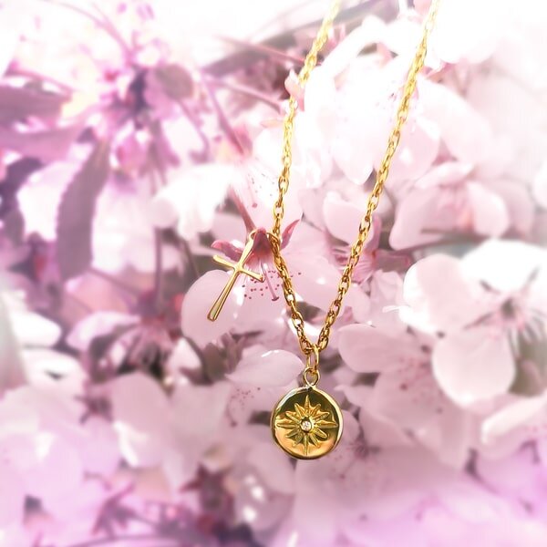 Goldfarbene Kette mit rundem Anhänger vor rosa Blüten