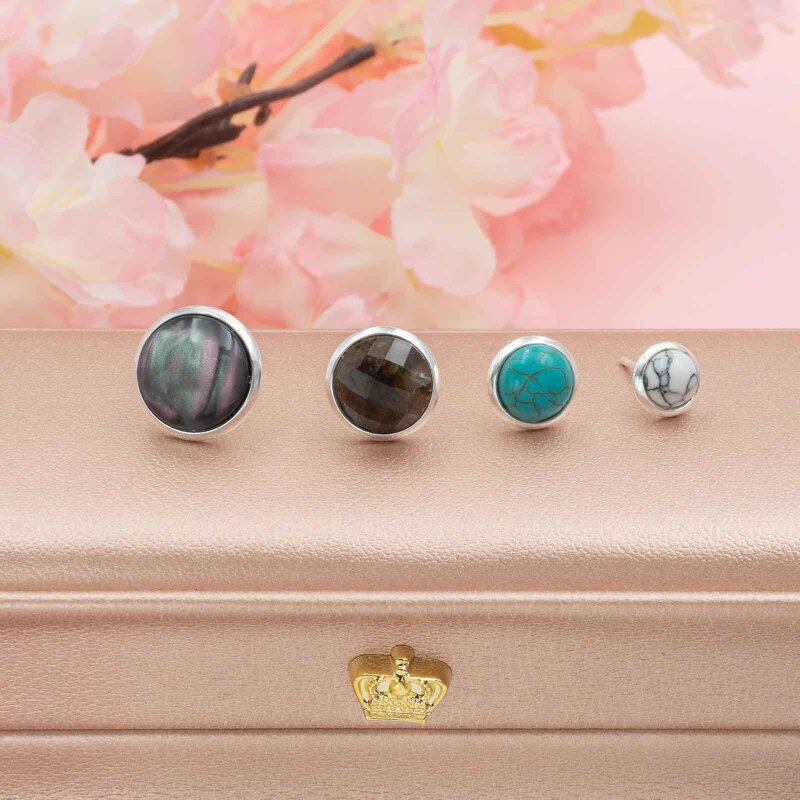 Vier silberfarbene Ohrstecker mit Cabochons vor Kirschblüten