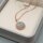 Fertiger Anhänger mit rundem Labradorit-Cabochon in roségoldfarbener Zargenfassung an einer feinen roségoldfarbenen Ankerkette, auf einem Schmuckkissen.