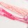 Geknüpftes Armband aus pinker Nylonkordel mit rosa Buchstabenwürfeln, daneben eine hellrosa Quaste und rosa Perlen auf hellem Stein. Die dicht gesetzten Makramee-Knoten und die losen Kordelenden sind sichtbar.