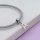 Graues geflochtenes Armband auf einer weißen Marmorplatte, darauf eine platinfarbene Collierschlaufe aufgefädelt. An ihrer unteren Öse hängt ein Buchstabenanhänger in Form eines A, das Band liegt in einer weichen Schlaufe.