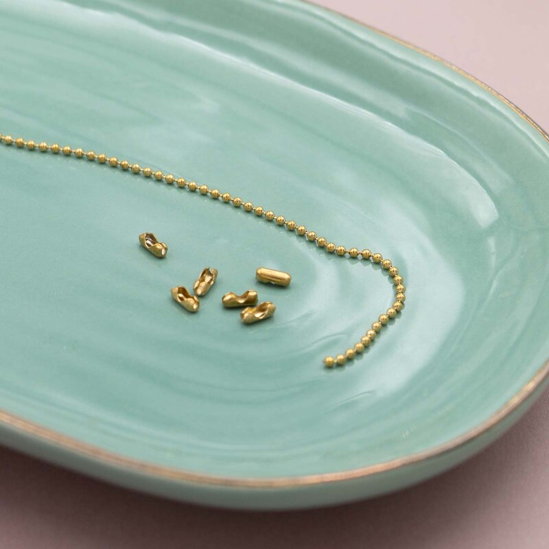 Goldfarbene Kugelkette mit Verschlüssen auf einer mintgrünen Keramikschale