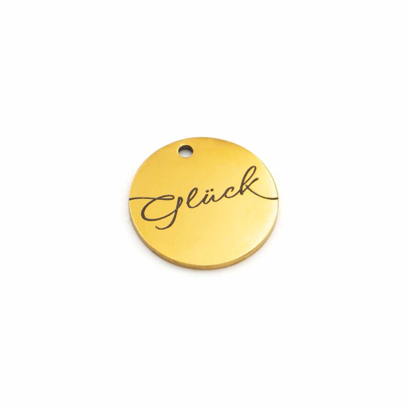 Runder Anhänger aus Edelstahl in Goldfarben mit Loch am oberen Rand, graviert mit dem Wort „Glück“ in geschwungener Schreibschrift, auf weißem Grund